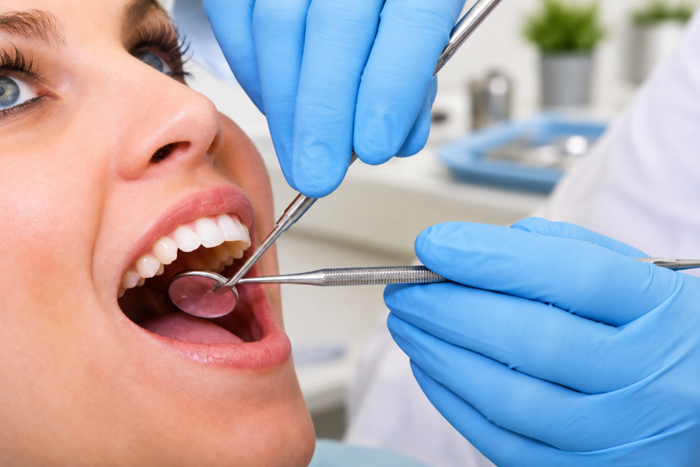 Routine Dental Exams Checkups in Northern Kentucky | Torbeck Dental Dentist in blue gloves examining a patient's open mouth with dental mirror and probing tools